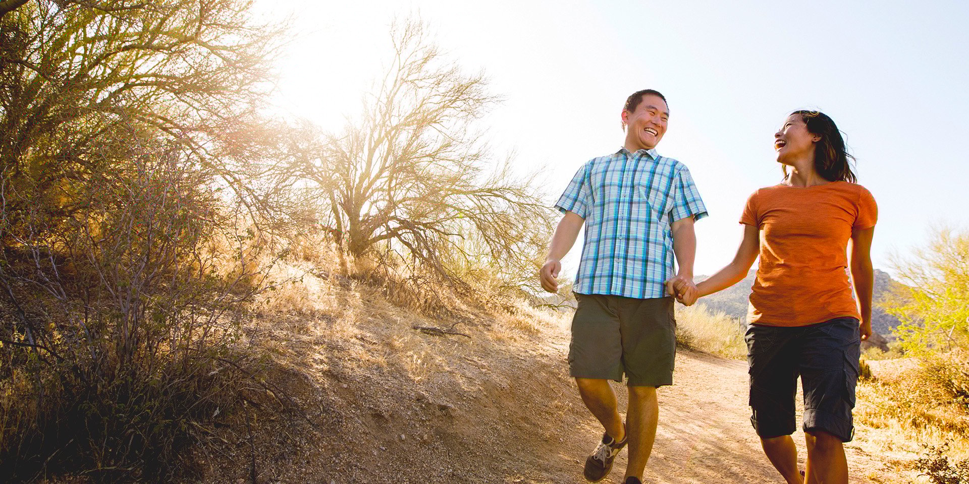 Happy couple holding hands while walking down a trail in the desert. 