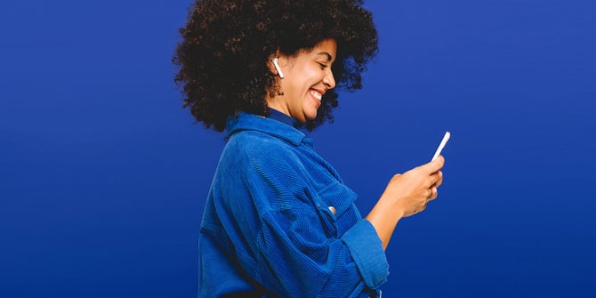 A happy woman in a blue shirt using her smartphone to access the checking features on the Desert Financial mobile banking app.