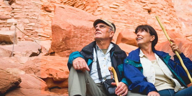 Mature couple rests post-canyon hike, admiring the beauty with walking sticks in hand.